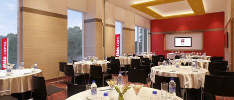 A conference room with multiple round tables, chairs, and a large screen for presentations.