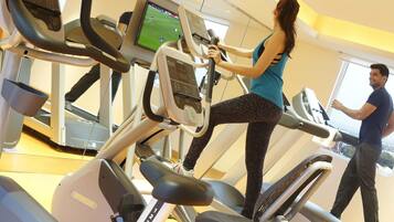 A gym with stationary bikes and a treadmill, a person using a bike, and another person standing by.