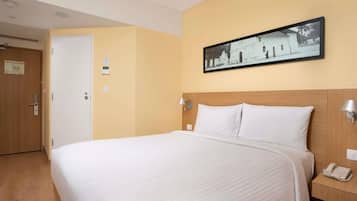 Una habitación de hotel con cama, mesita de noche con teléfono, un cuadro en la pared y una puerta con un letrero.