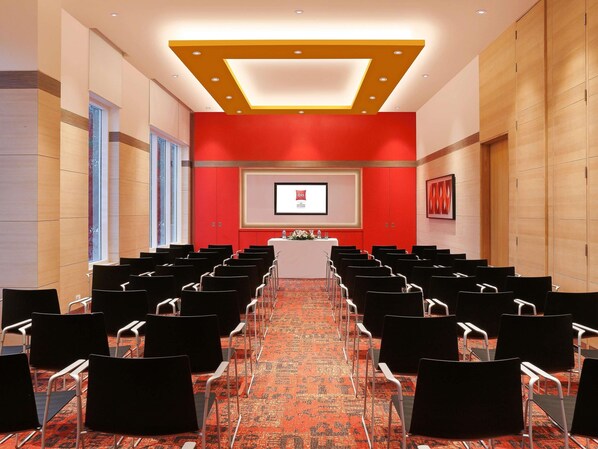 A conference room with rows of chairs, a podium, and a screen displaying a logo.