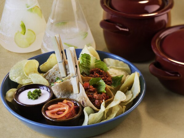 A bowl of food with chips, a drink, and a sauce.