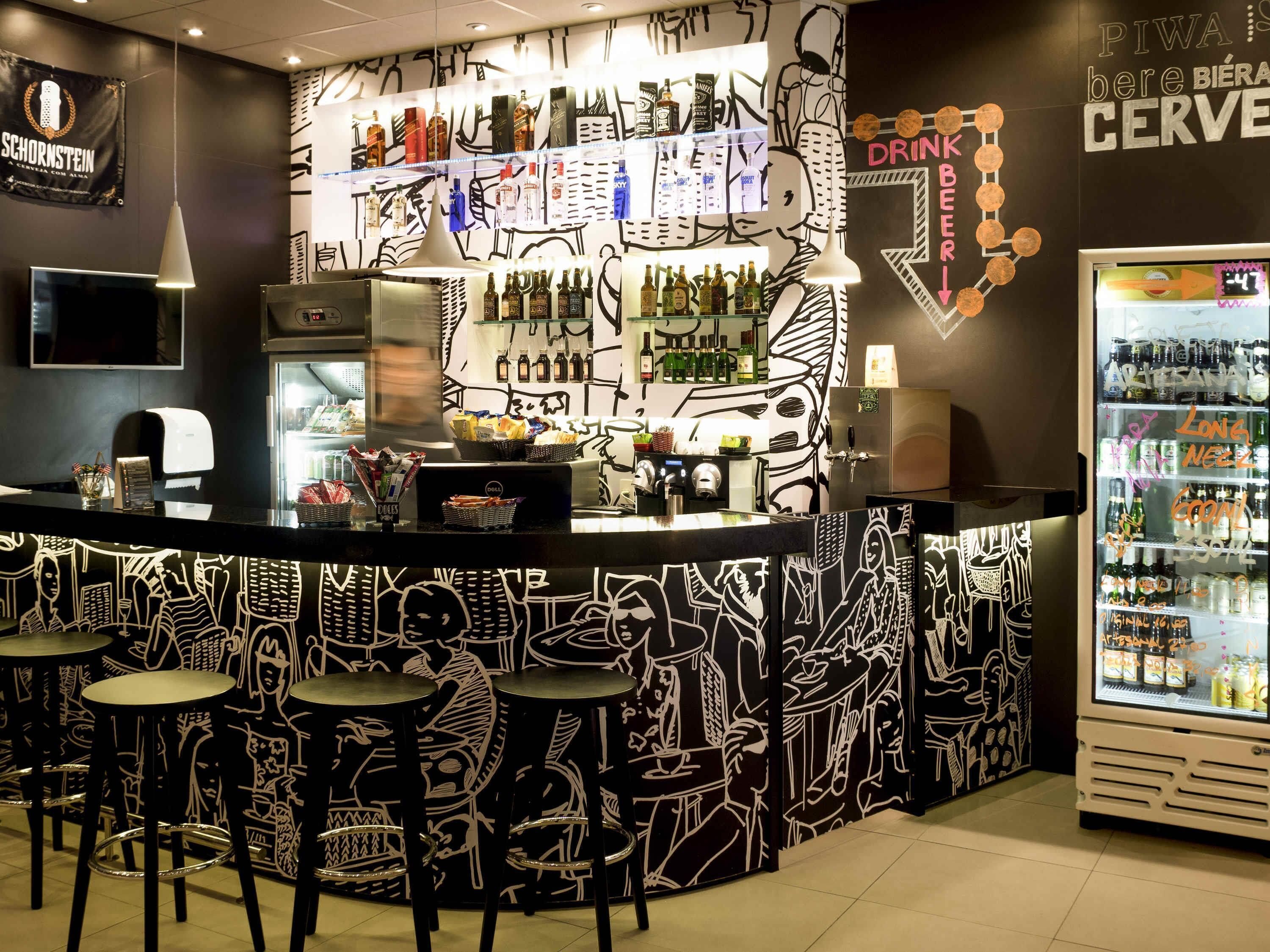 Angolo bar con bancone, sgabelli e frigorifero pieno di bevande.