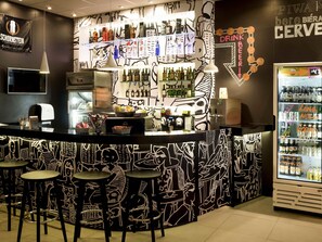 Zona de bar con mostrador, taburetes y refrigerador lleno de bebidas.