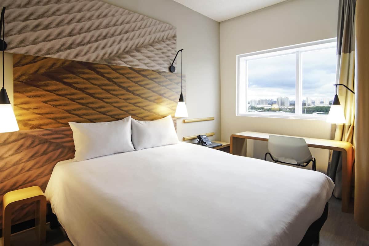 Hotellihuone, jossa on suuri sänky, työpöytä, tuoli, puhelin ja ikkuna, josta on näkymä kaupunkiin.