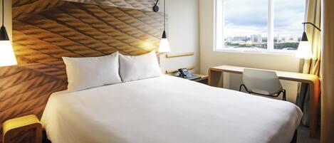 Et hotelværelse med en stor seng, et skrivebord, en stol, en telefon og et vindue med udsigt over byen.