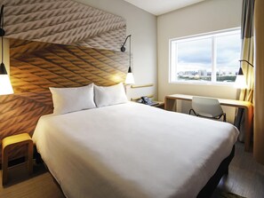 Habitación de hotel con una cama grande, un escritorio, una silla, un teléfono y una ventana con vista a la ciudad.