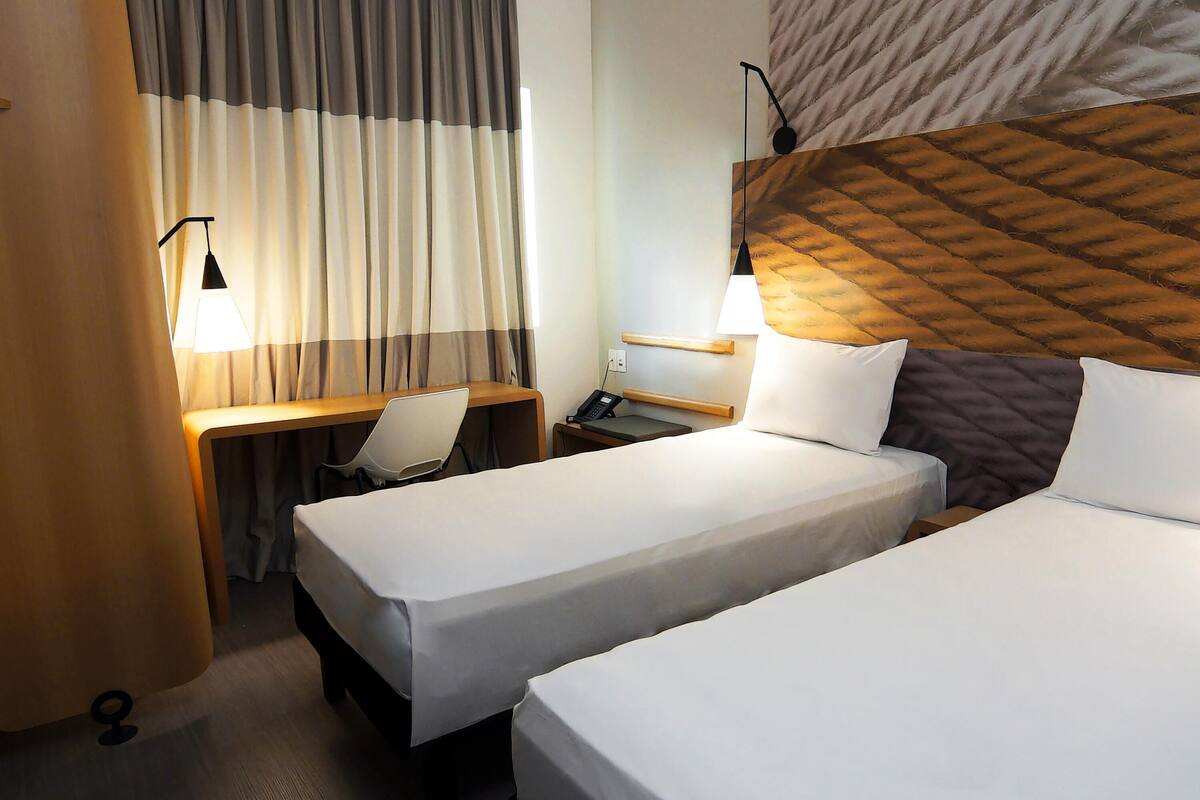 A hotel room with two beds, a desk, a chair, a lamp, and a telephone.
