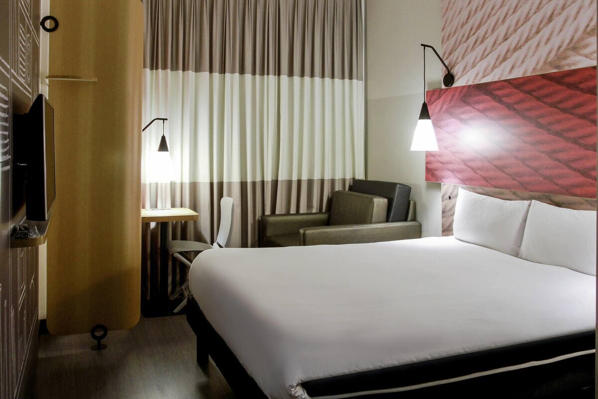 A hotel room with a bed, a desk, a chair, and a TV.