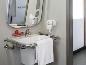 A bathroom with a white sink, a handheld hair dryer, and a towel hanging on the side. - Ibis Osasco (Osasco)