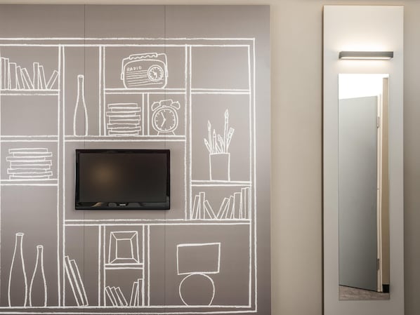 A wall with a flat-screen TV mounted above a chalkboard-style wall art depicting various objects like books, a radio, and a clock.