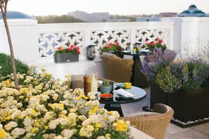 An outdoor patio with wicker furniture, a round table, and potted plants with flowers. - Hyatt Regency Tashkent (Tashkent)