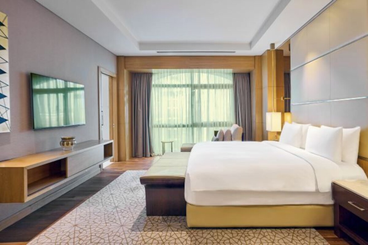 A modern hotel room with a large bed, a flat-screen TV, a bedside table, and a window with curtains.