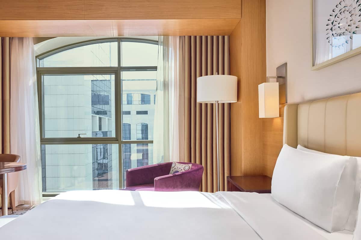 Una habitación de hotel con una cama grande, una mesita pequeña, una silla y una ventana con cortinas.