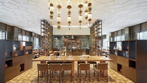Un espace de restauration moderne avec un sol à carreaux, une longue table en bois dressée pour quatre personnes et des lustres en cristal suspendus au plafond.
