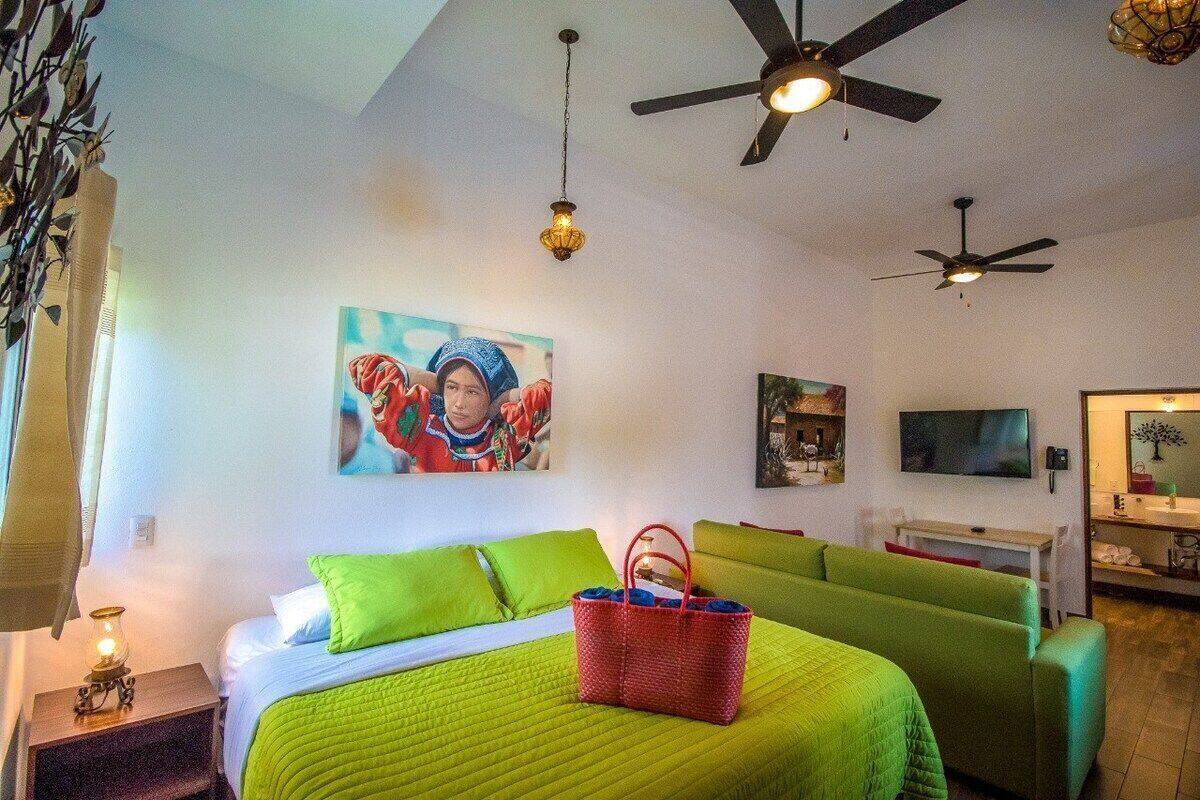Ein Zimmer mit einem Bett, einem grünen Sofa, einem roten Korb und zwei Deckenventilatoren.