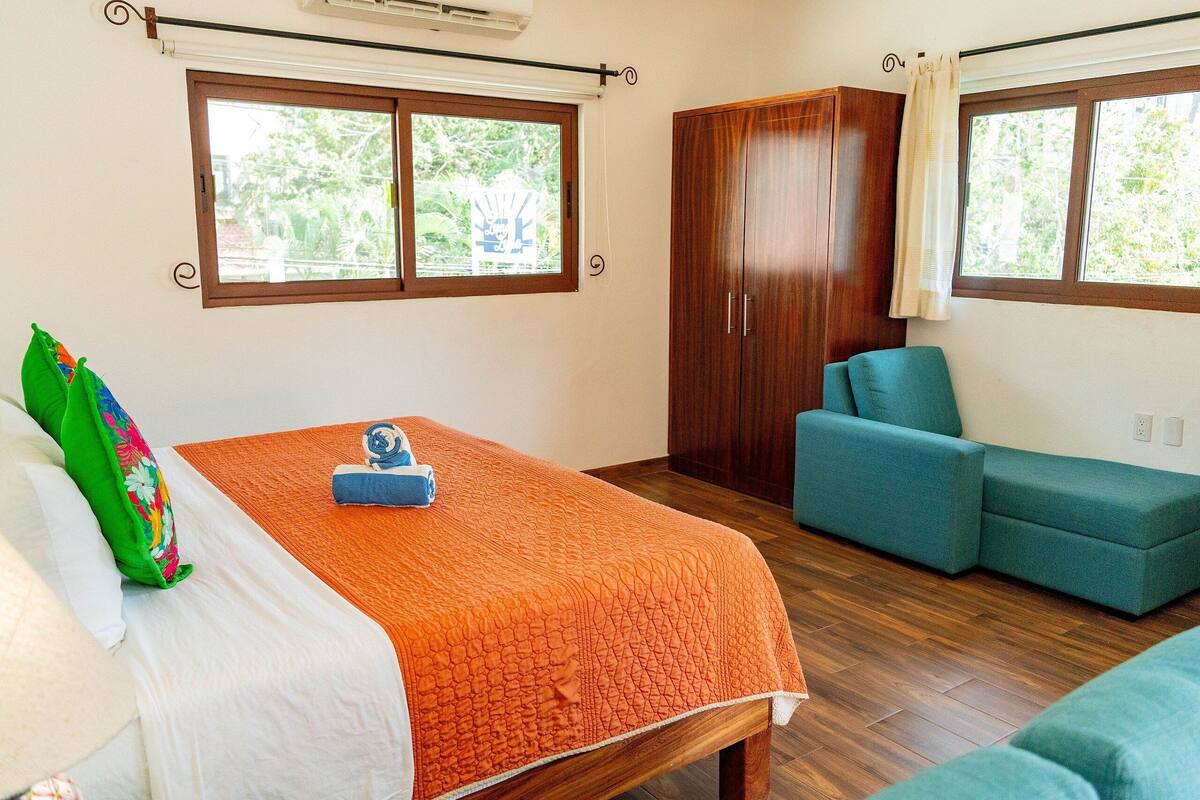 Ein Schlafzimmer mit einem Bett, einem Holzschrank und einem blaugrünen Sofa.