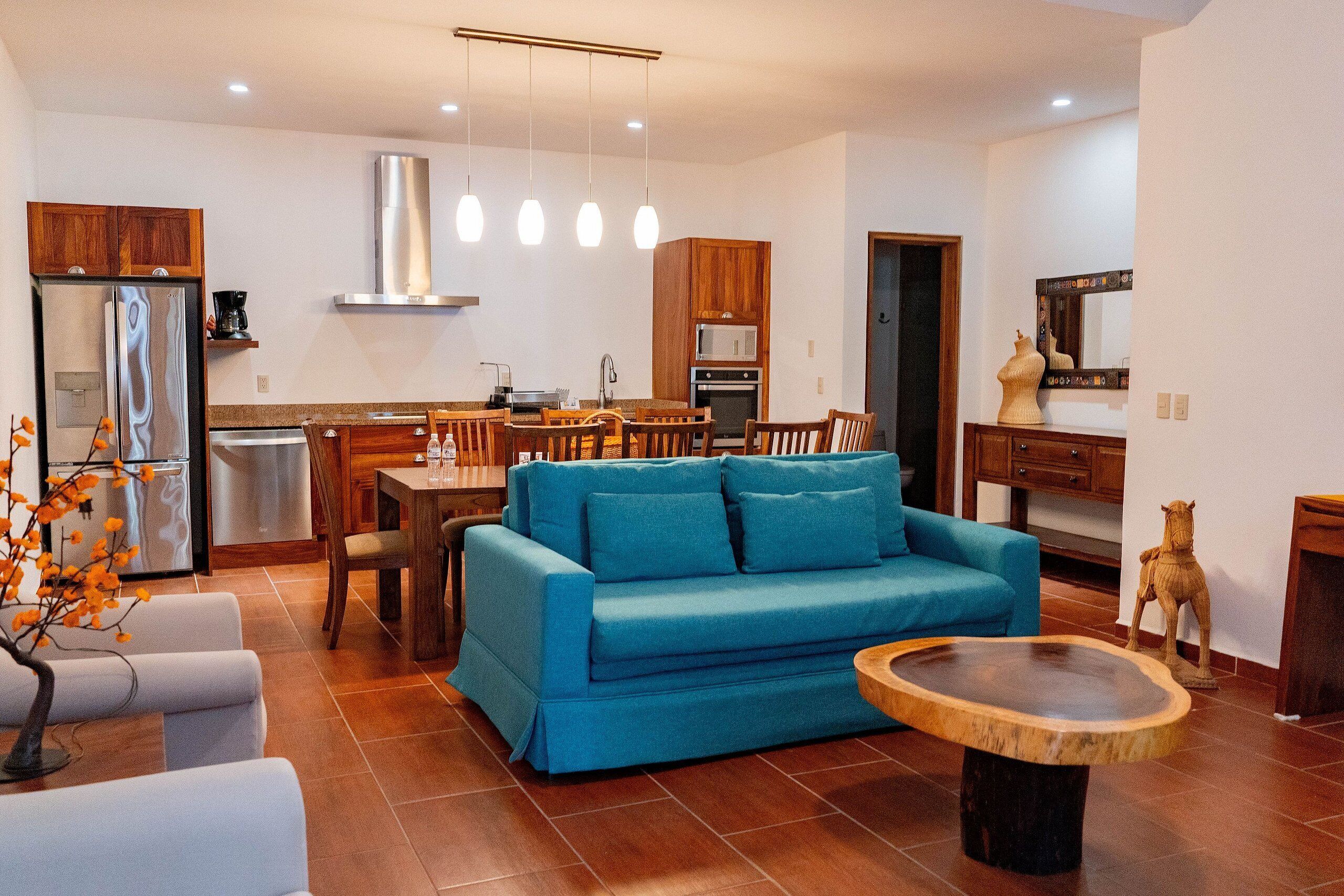 Un salon moderne avec un canapé bleu, une table à manger en bois et un coin cuisine équipé d’appareils électroménagers en acier inoxydable.