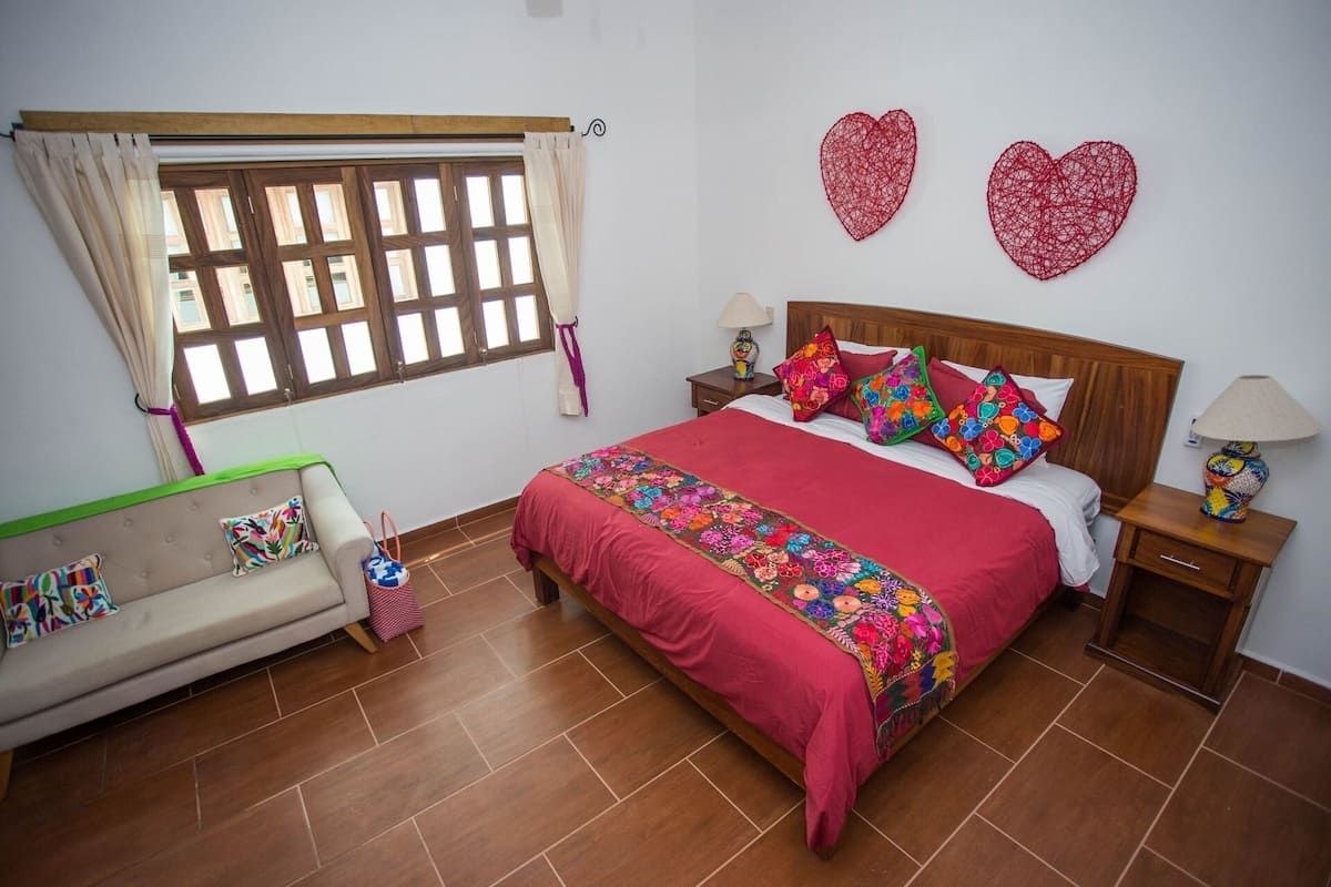 Ein Schlafzimmer mit einem Bett, einem Schlafsofa, einem Fenster mit Vorhängen, einem Nachttisch und einer Wand mit zwei Herzdekorationen.
