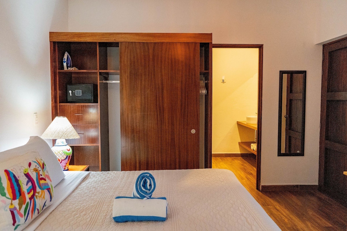 Ein Hotelzimmer mit einem Bett, einem Holzschrank, einem Nachttisch mit Lampe und einem durch eine offene Tür einsehbarer Badezimmer.