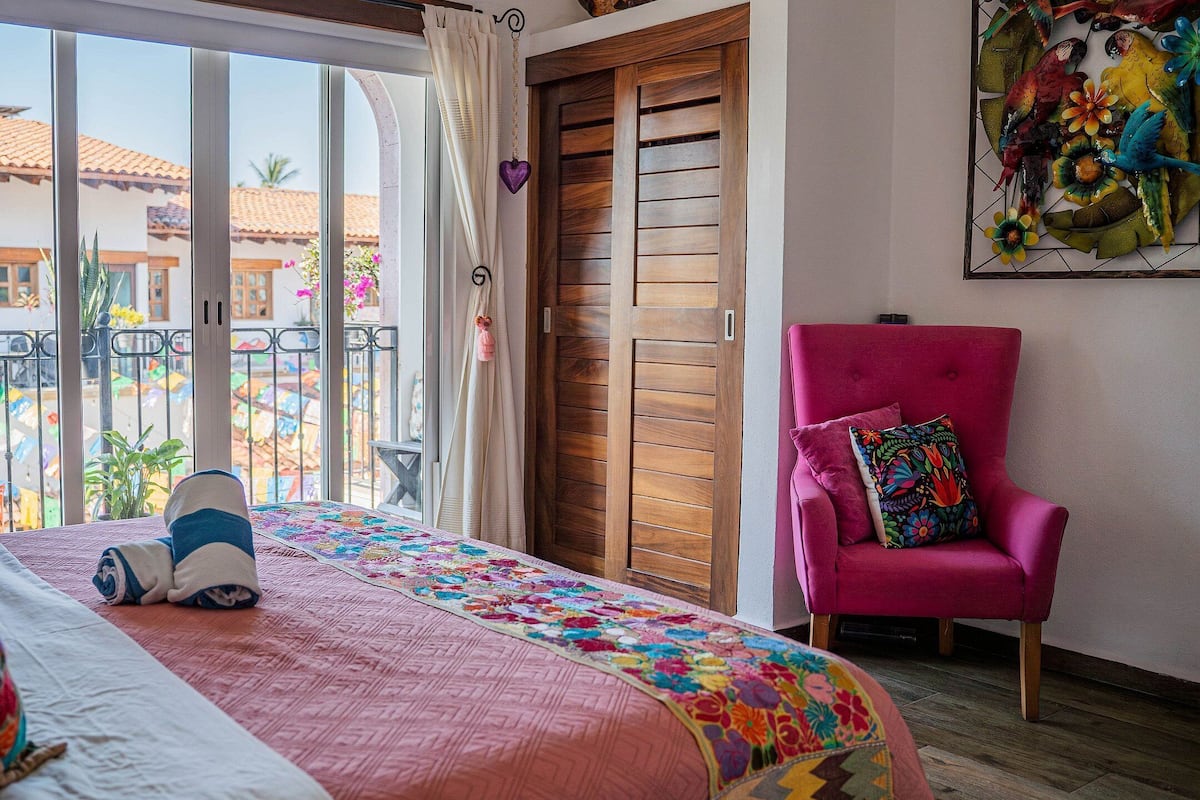 Ein Schlafzimmer mit einem Bett, einem rosa Sessel und Blick auf einen Innenhof mit Flaggen.