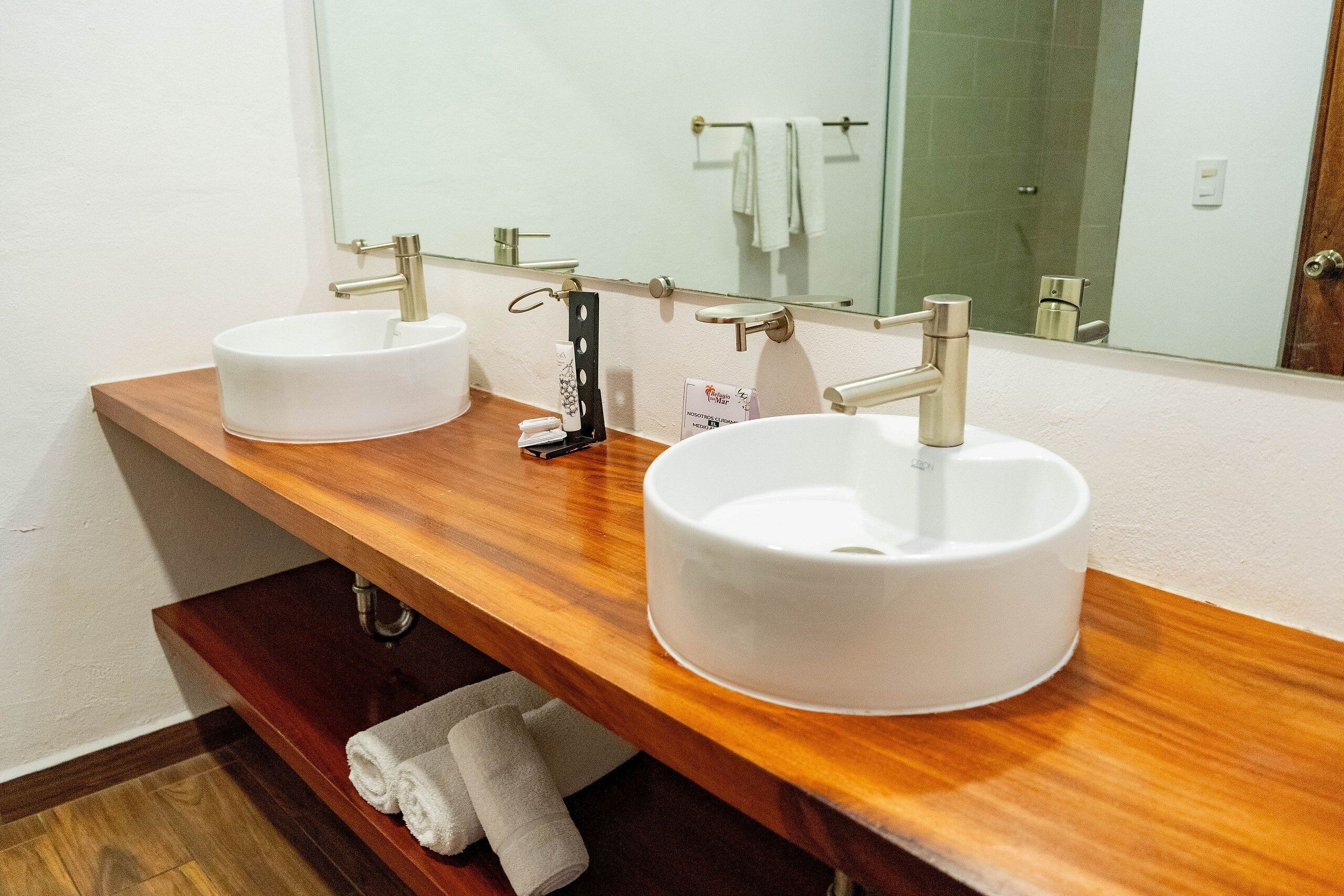 Un baño con dos lavamanos blancos, un mueble de tocador de madera, un espejo y un perchero para toallas.