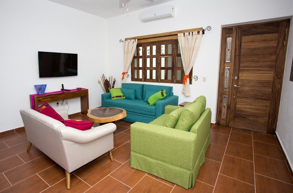 Una sala de estar con sofá, sillón y televisor montado en la pared.