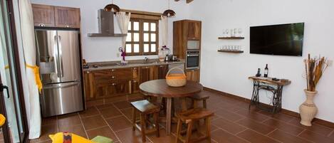 A compact kitchen with modern appliances, a dining area with wooden furniture, and a flat-screen TV mounted on the wall.