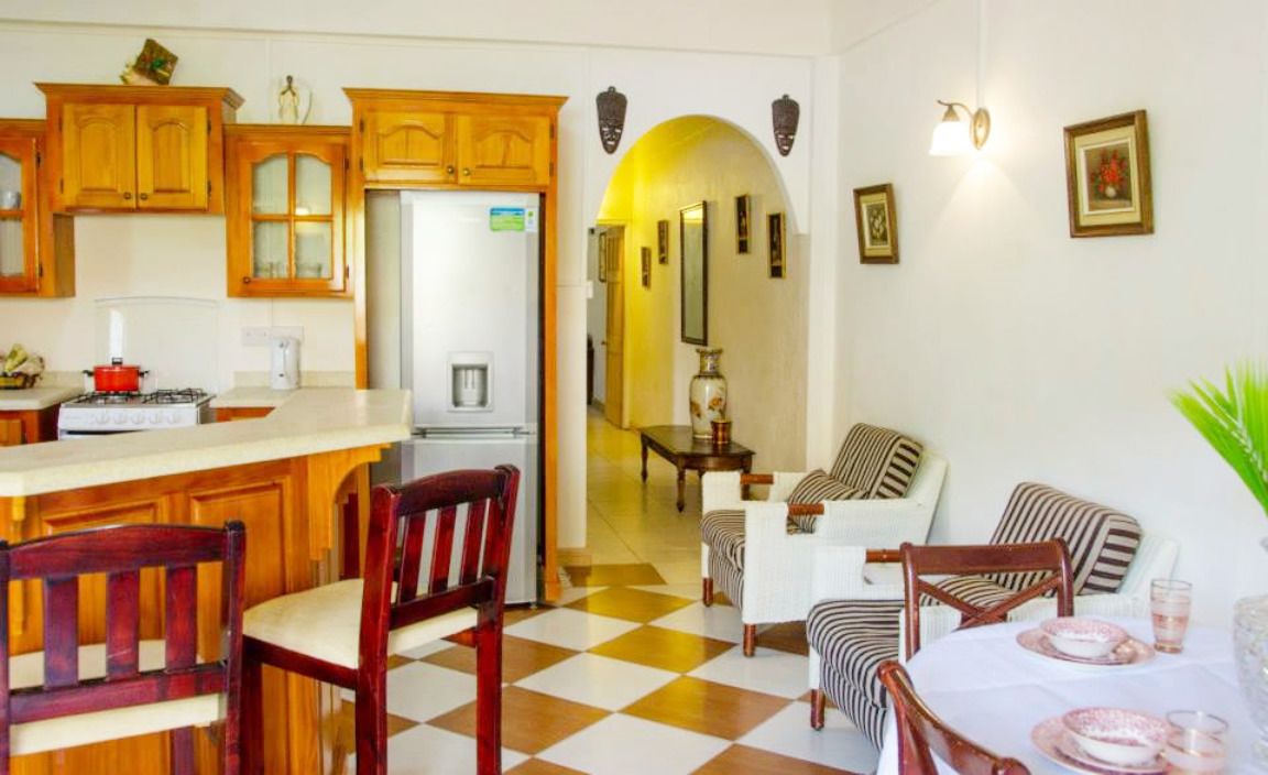 Una cocina con armarios de madera, una zona de comedor con sillas a rayas y un suelo a cuadros.