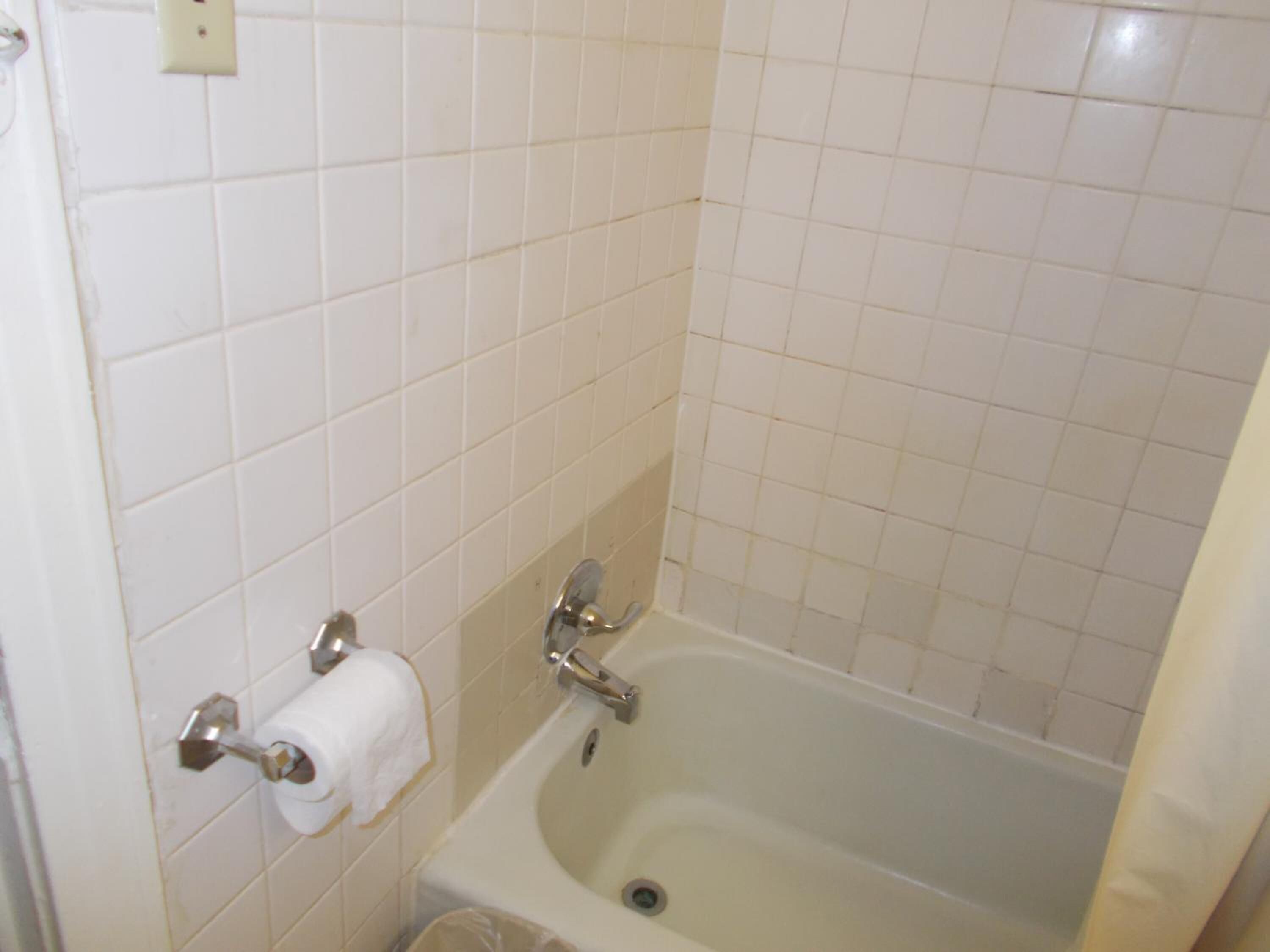 A bathroom with white tiled walls, a bathtub, a toilet, and a towel rack.