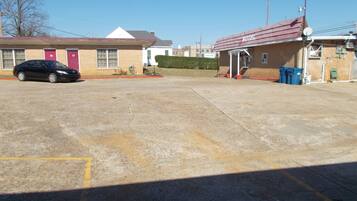 A parking lot with a black car parked in front of a building with a red door labeled "16".