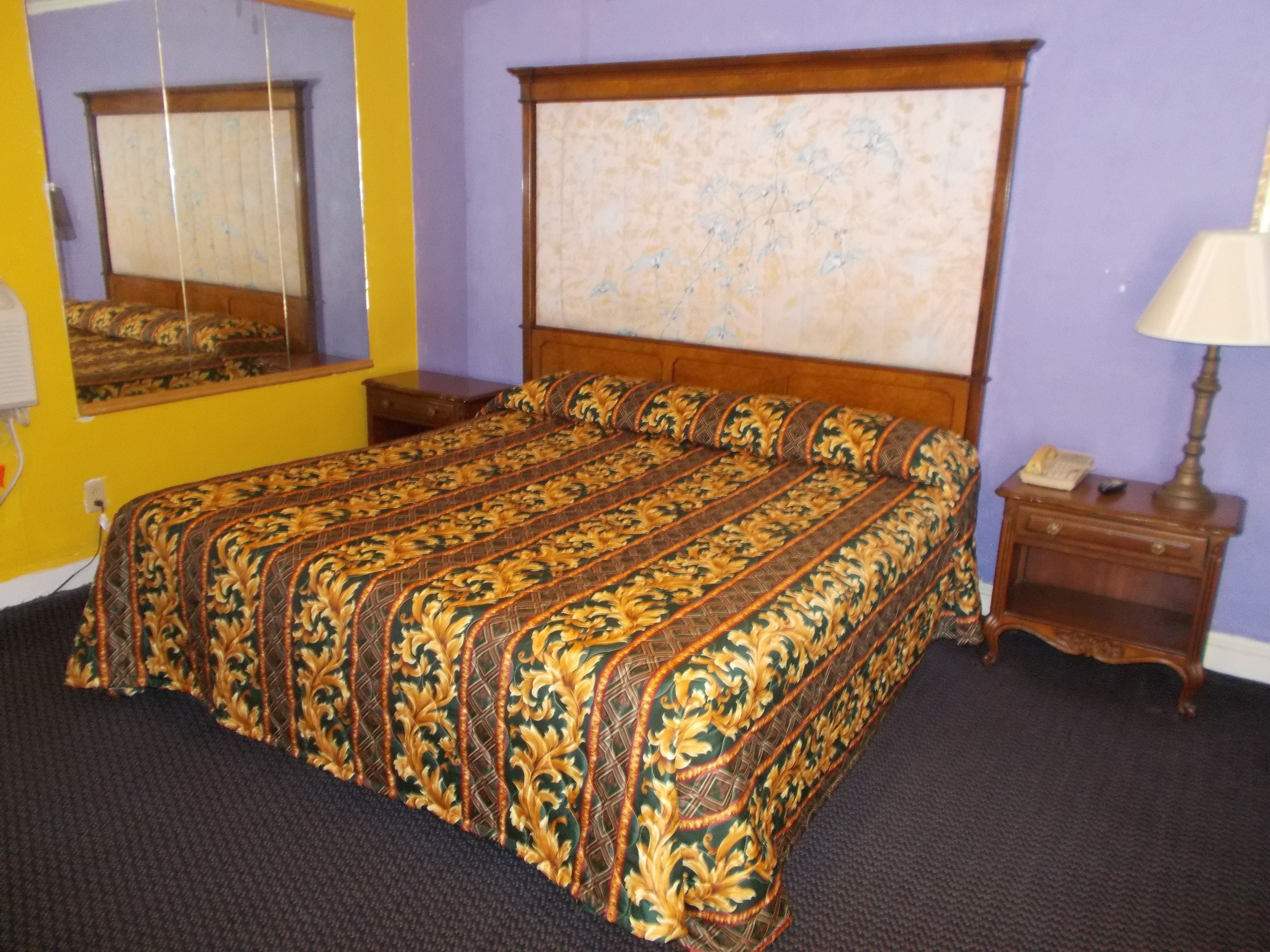 Une chambre à coucher avec un grand lit, une tête de lit en bois, une table de chevet, une lampe et un miroir.