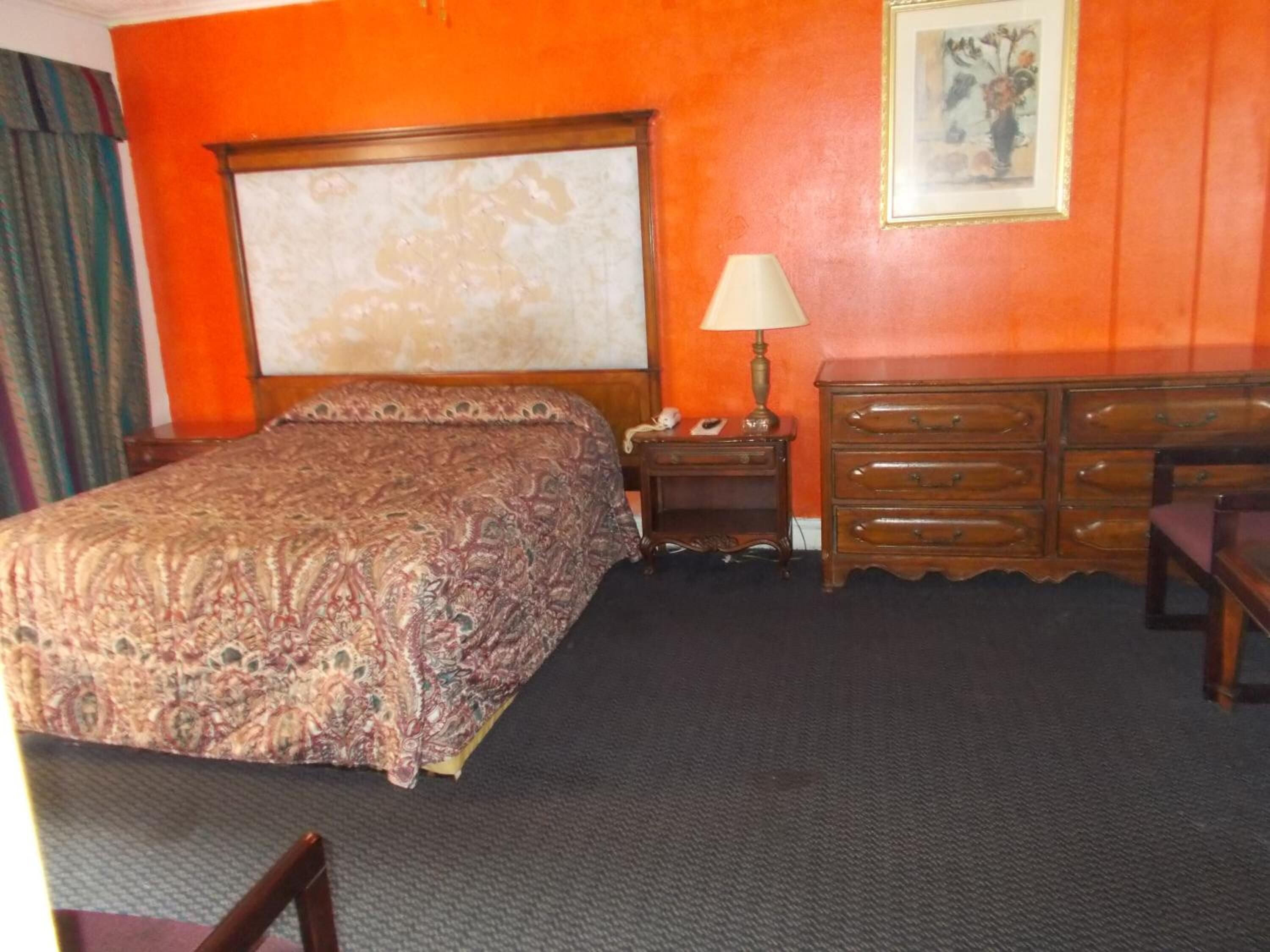 A hotel room with a large bed, a nightstand with a lamp, a dresser, and a framed picture on the wall.