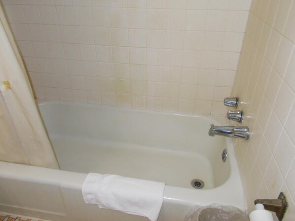 A bathtub with a white towel hanging on the side, a showerhead, and a drain. - Hillside Motel (Homer)