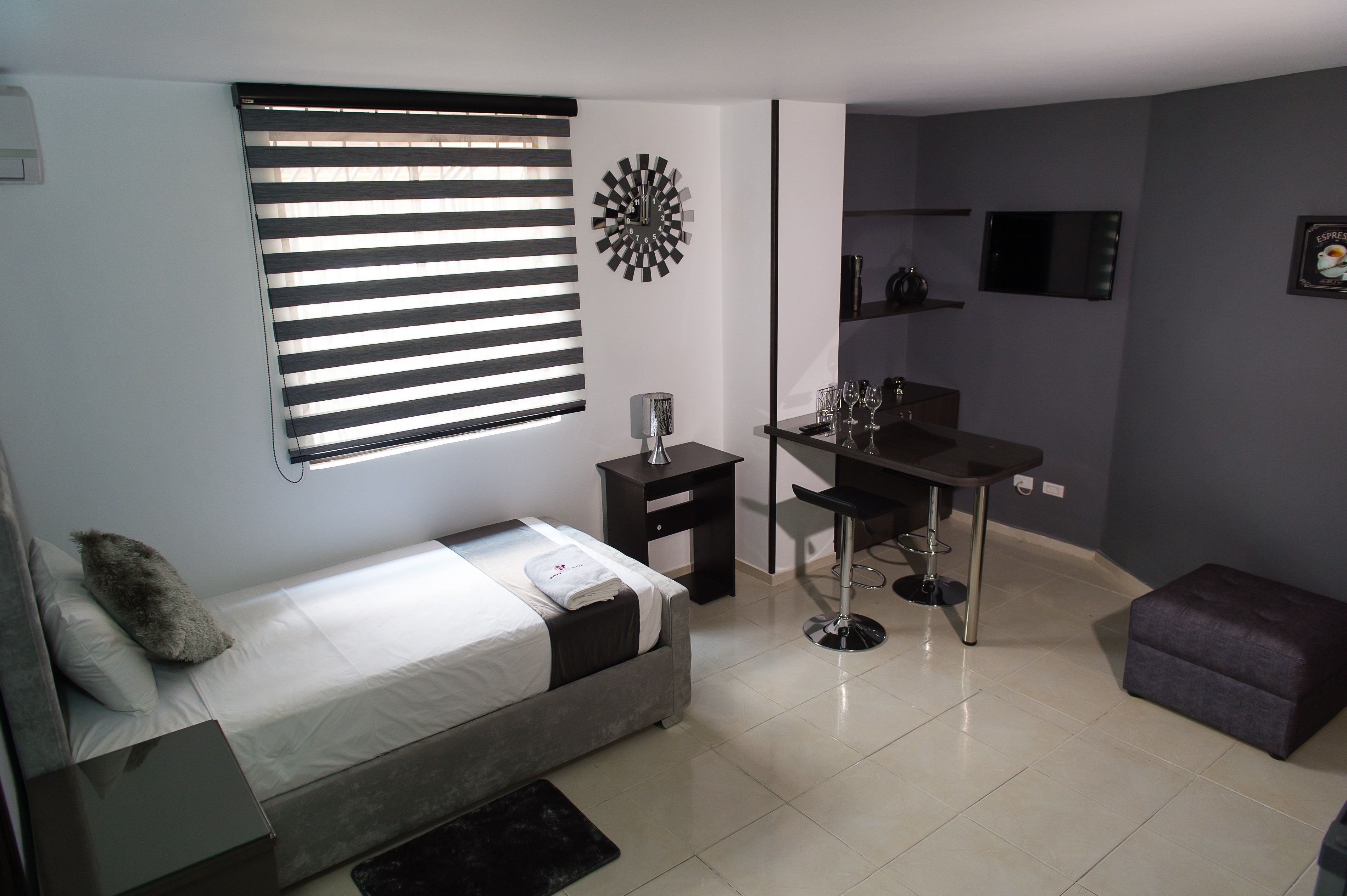 A compact room with a bed, a desk, and a small stool.