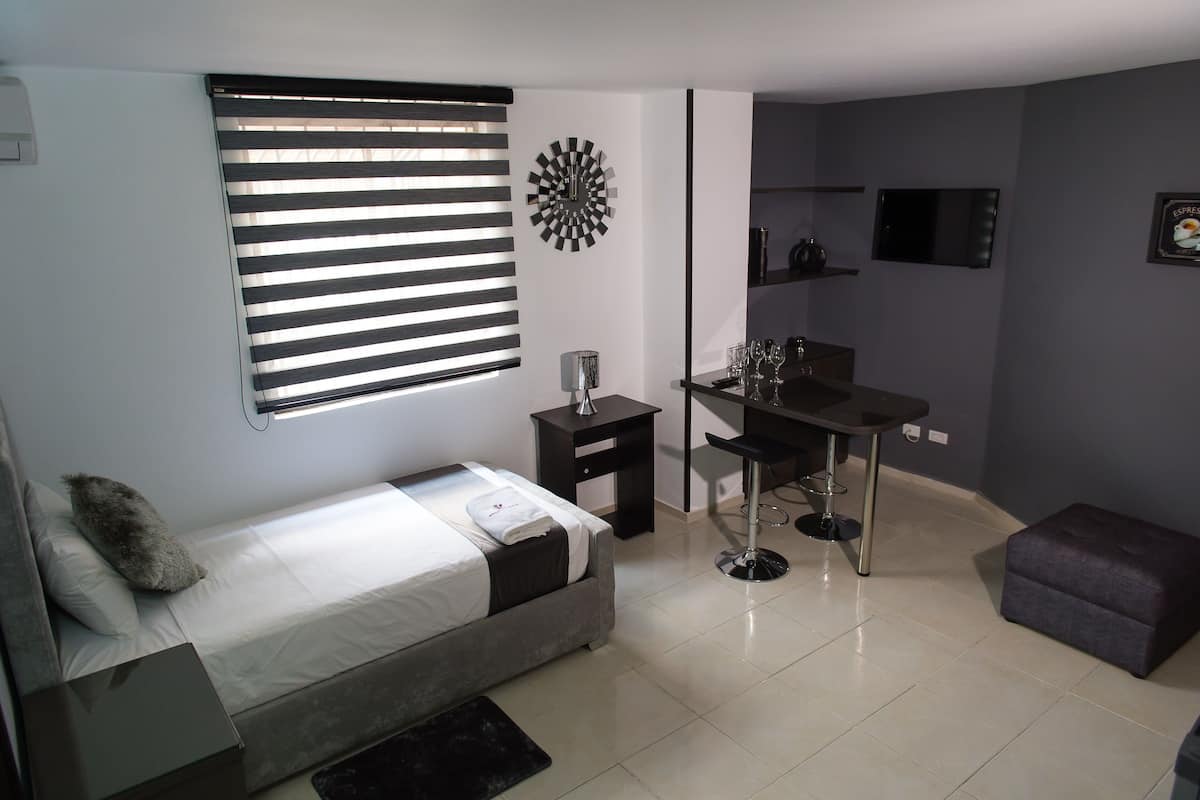 A compact room with a bed, a desk, and a small stool.