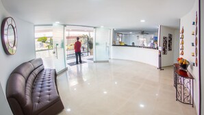 A spacious lobby with a leather sofa, a reception desk, and a glass door leading outside. - Hotel Roosevelt Plaza (Cali)