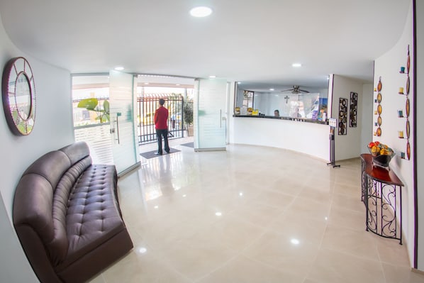 Un hall d’entrée spacieux, avec un canapé en cuir, un comptoir de réception et une porte vitrée donnant sur l’extérieur.