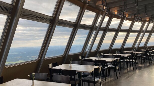 A restaurant with large windows offering a view of the landscape. Tables and chairs are arranged for dining.