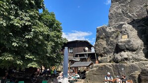 An outdoor seating area with tables and chairs, a large rock formation, and a building with a sign.