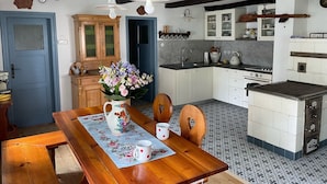 A kitchen with white cabinets, a wooden table with a floral tablecloth, and a vase of flowers.