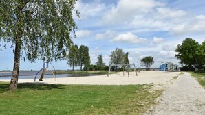 A sandy beach area with a playground, a small blue building, and a path leading to it.
