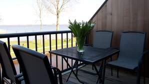 An outdoor deck with a table and chairs, a vase of flowers, and a view of a body of water and trees.