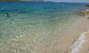 Une plage publique avec une eau claire, des gens qui se baignent et une rive sablonneuse.