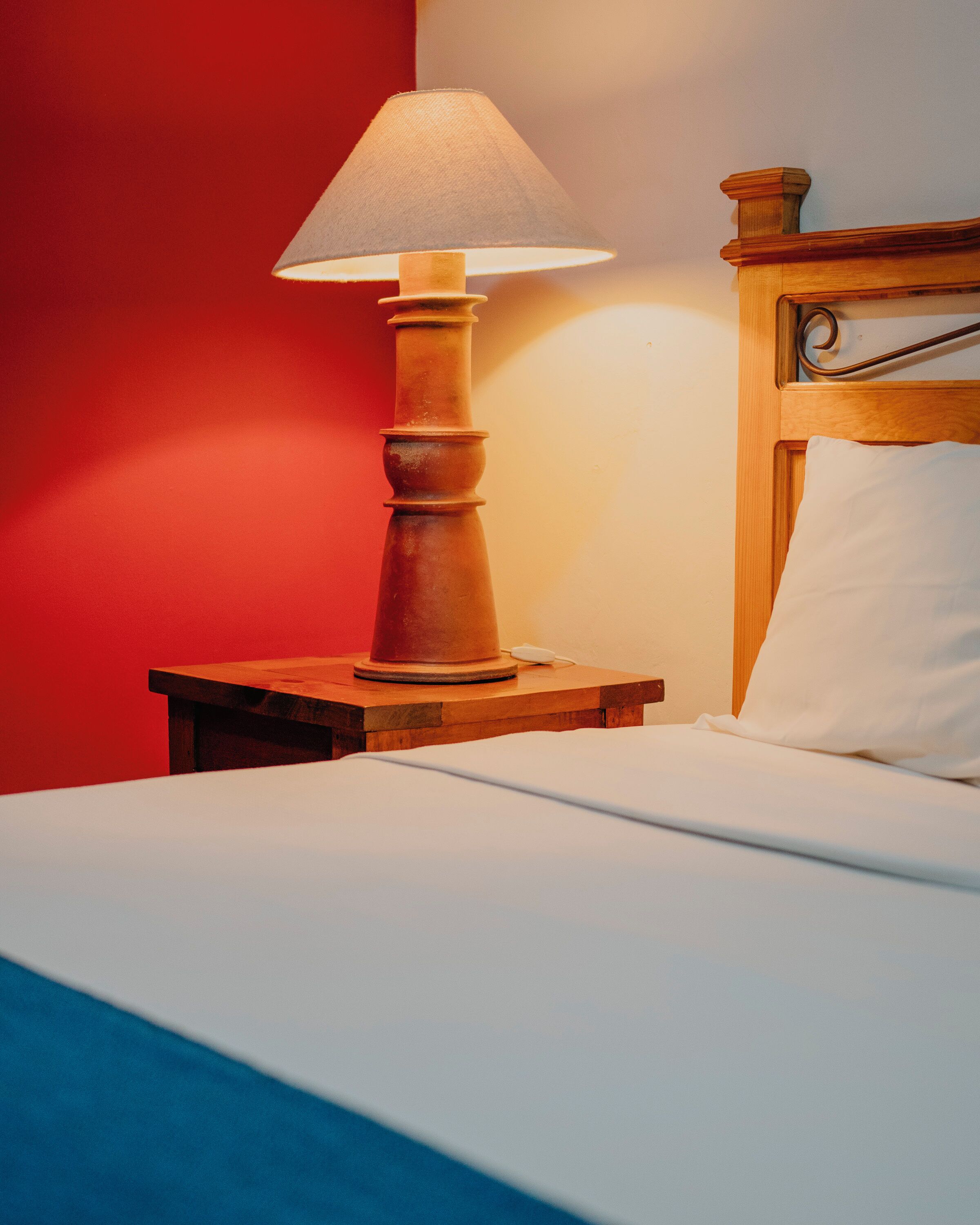A bed with a wooden headboard, a bedside table with a lamp, and a red wall.