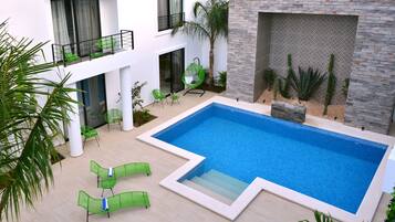 A modern outdoor pool area with a rectangular pool, green lounge chairs, and a palm tree.
