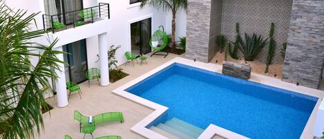 A modern outdoor pool area with a rectangular pool, green lounge chairs, and a palm tree.