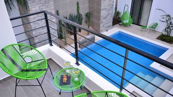 Un balcón con piscina, sillas verdes y una mesa con bebidas.