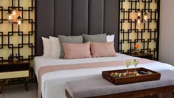 Una cama bien hecha con almohadas, una mesita de noche, una bandeja con bebidas y sushi, y un panel decorativo en la pared.