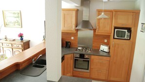 A compact kitchen with wooden cabinets, a gas stove, an oven, a microwave, and a toaster. - Cozy Garden Home in Erquy (Erquy)
