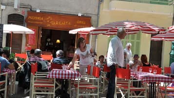 Ulkoilma-alue, jossa on punavalkoruutuisia pöytiä ja tuoleja, pizzaravintolan kyltti ja grillin kyltti.